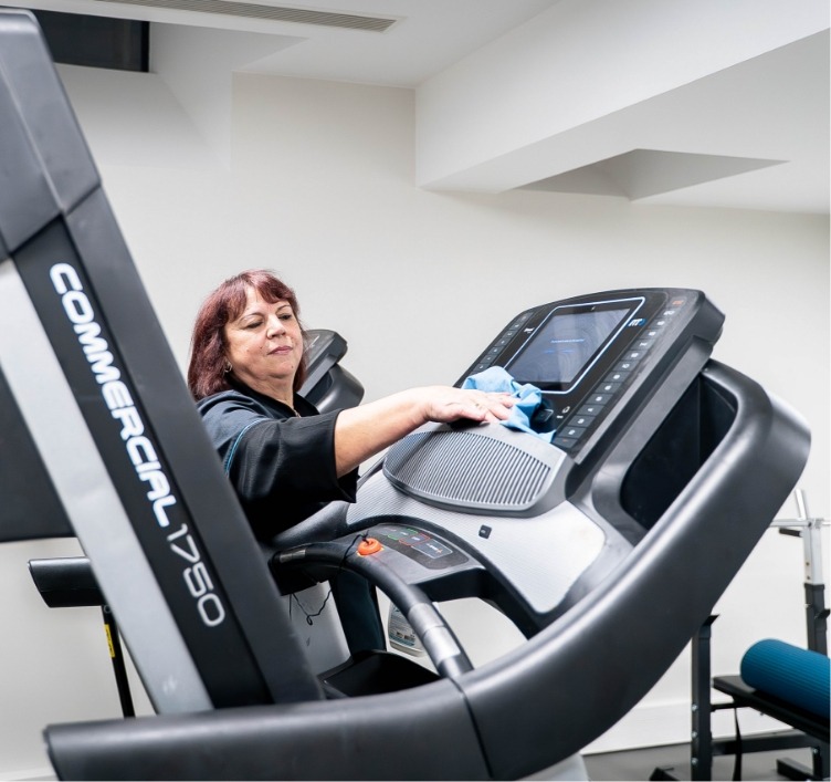 Agent de ménage Adapt propreté qui nettoie un tapis de course.